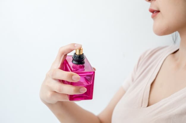 Mujer rociandose perfume de bote rosa